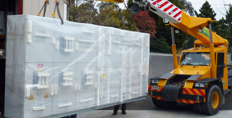 Crane lifting a wrapped switchboard cabinet for delivery to site